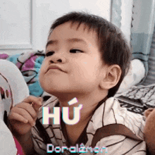 a little boy is making a funny face while sitting on a bed with the word hu on his face .