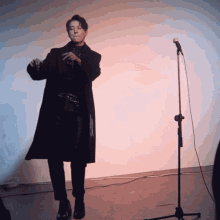 a man in a black coat stands in front of a microphone with his hands in his pockets