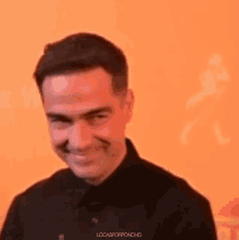 a man in a black shirt is smiling against an orange background .