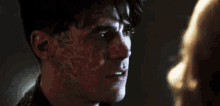 a man with scars on his face is looking at a woman in a dark room .