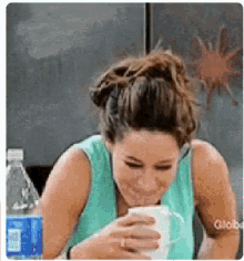 a woman laughs while drinking from a coffee mug
