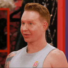 a man wearing a gray tank top with a rolling stones pin on it