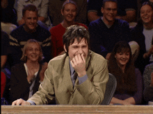 a man laughs while sitting in front of a crowd