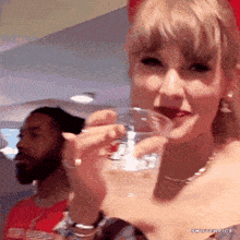 a woman is holding a glass of water in her hand while a man stands behind her