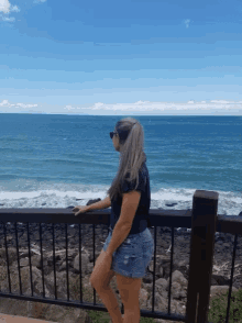 a woman leans on a railing looking out over the ocean