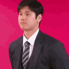 a young man wearing a suit and tie is standing in front of a red background .