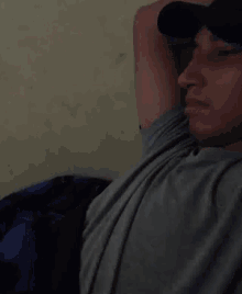 a man wearing a hat and a gray shirt is laying down on a bed .