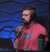 a man wearing headphones and a pink shirt with a dinosaur on it is sitting in front of a microphone