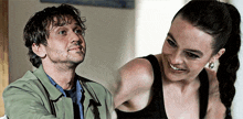 a man in a green jacket and a woman in a black tank top smile for the camera