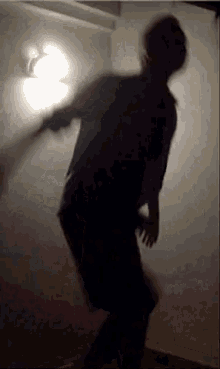a person is dancing in a dark room with a light on the wall