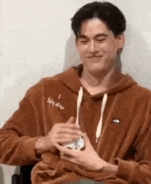 a young man in a brown hoodie is holding a card in his hand .