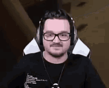 a man wearing glasses and headphones is sitting in a chair and smiling .