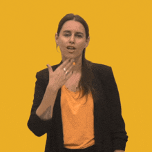a woman wearing an orange shirt and a black jacket is pointing her finger up