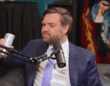 a man in a suit and tie is talking into a microphone while holding a can of soda .