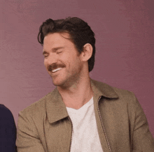 a man with a mustache is smiling and wearing a jacket