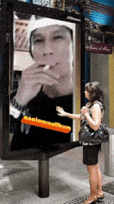a woman stands in front of a large billboard that says assalamualikum