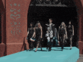 a group of people walking on a blue carpet in front of a building