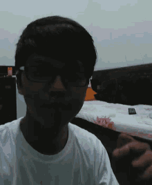 a young man wearing glasses and a white shirt is sitting in front of a bed