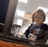 a doll is sitting in front of a window holding a drink and a straw .