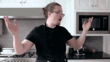 a man in a black shirt and apron is standing in a kitchen with his arms outstretched