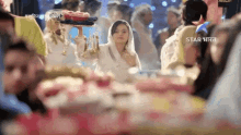 a woman in a white veil stands in a crowd with a star india logo on the bottom