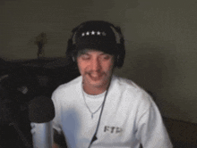 a man wearing headphones and a ftp shirt smiles in front of a microphone .