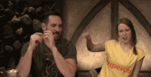 a man and a woman are sitting at a table and the woman is wearing a yellow shirt with the word super on it