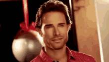 a man in a red shirt is smiling in front of a christmas tree ornament .