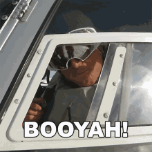 a man wearing goggles looks out of a window with the words booyah written on it