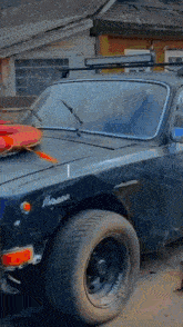 a black car with a surfboard on top of it is parked in front of a building .