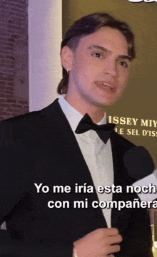 a man wearing a tuxedo and bow tie is speaking in spanish