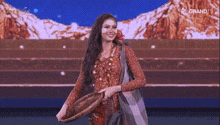 a woman in a red dress is standing on a stage holding a basket and smiling .