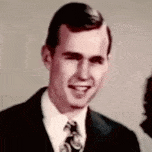 a man in a suit and tie is smiling in a black and white photo .