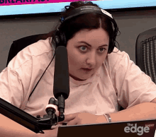 a woman wearing headphones sits in front of a microphone that says the edge on it