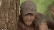 a man is holding a gun in front of a tree .