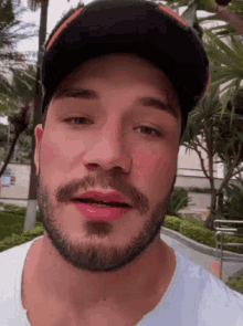 a man with a beard wearing a baseball cap and a white shirt .