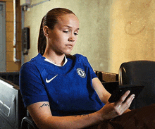 a woman wearing a blue nike shirt is sitting in a chair looking at her phone