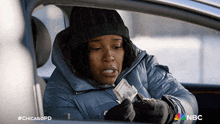 a woman is sitting in a car holding a piece of paper with the nbc logo on it