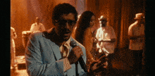a man in a suit is singing into a microphone in front of a group of people