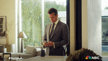 a man in a suit and tie is standing in front of a nbc advertisement
