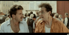 a man with a mustache is talking to another man in front of a crowd of people