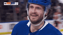 a hockey player wearing a blue helmet is smiling in front of a scoreboard that says sm on it