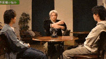 three men are sitting at a table in a living room talking to each other .