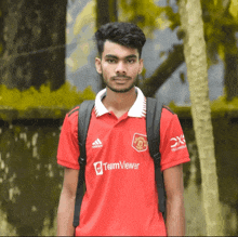 a man wearing a red teamviewer shirt stands in front of trees