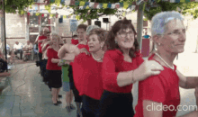 a group of older women in red shirts are dancing in a row