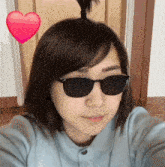 a woman wearing sunglasses takes a selfie with a heart in the background