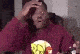 a man in a red hoodie is sitting on a couch holding his head .