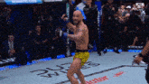 a man in yellow shorts is standing in a boxing ring with the word ufc on the floor