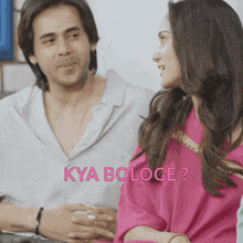 a man and a woman are sitting next to each other and the woman is wearing a pink shirt that says kya bologe ?