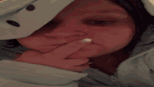 a woman covering her mouth with her finger and wearing a light blue hoodie